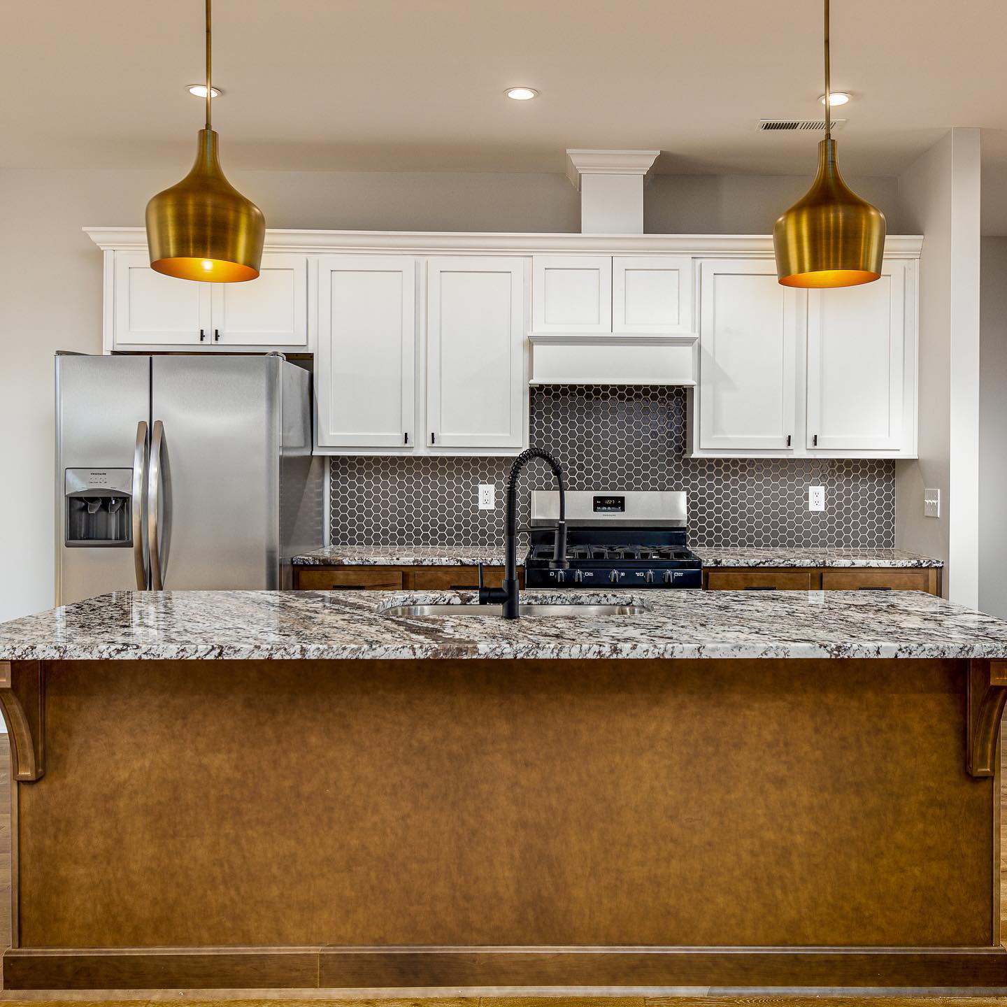 Kitchen with brass pendants, granite island, and hex tile backsplash